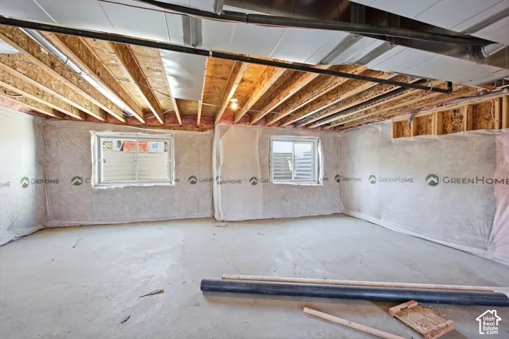Unfinished basement with exposed wood joists and concrete flooring, featuring two windows with white grilles