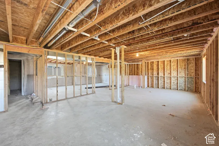 Unfinished basement space featuring exposed wood framing, concrete flooring, visible ceiling joists, and plumbing conduit