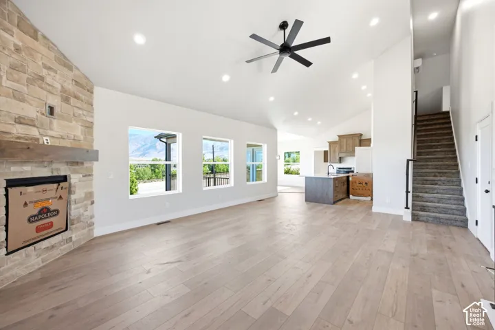Spacious open-concept living area featuring light wood-finish flooring and a stone-clad fireplace with a wood mantel
