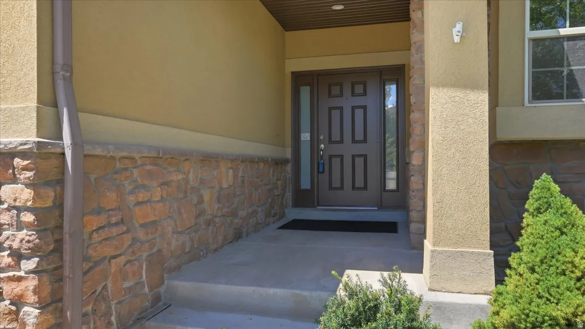Entryway featuring a panel door with sidelights, a textured stucco exterior, and a stone veneer foundation
