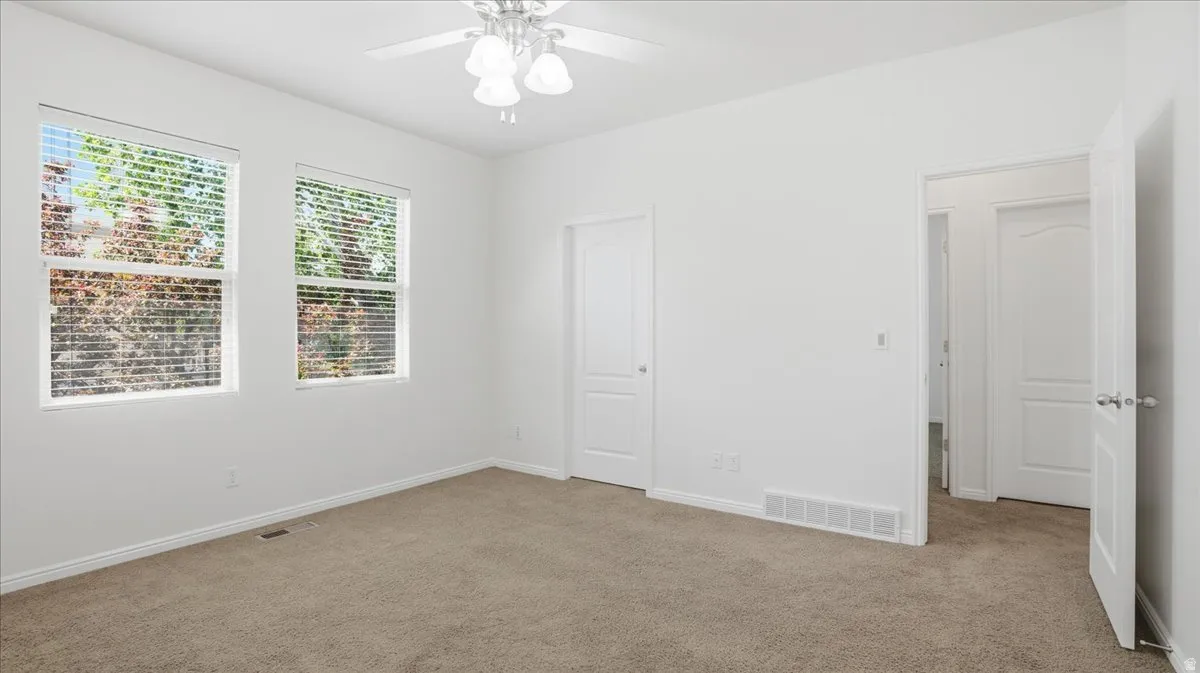 Carpeted interior space featuring two windows with horizontal blinds, a white ceiling fan with light fixture, and white painted walls