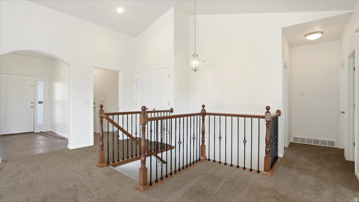 Hall featuring carpet, an upstairs landing, lofted ceiling, and arched walkways