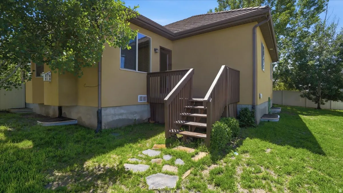 Rear exterior featuring a wood-toned deck with stairs, stucco siding, and a partial stone pathway