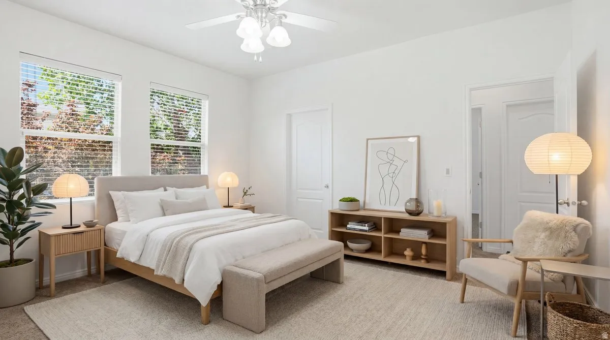 Bright bedroom featuring two windows with blinds, a ceiling fan with integrated lighting, a built-in shelving unit, and two panel doors