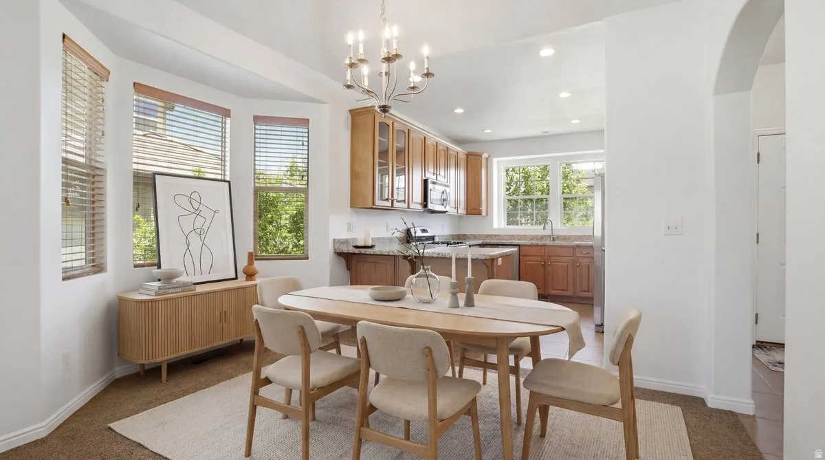 Dining area with an elegant chandelier, wood-finish flooring, and a bay window featuring horizontal blinds