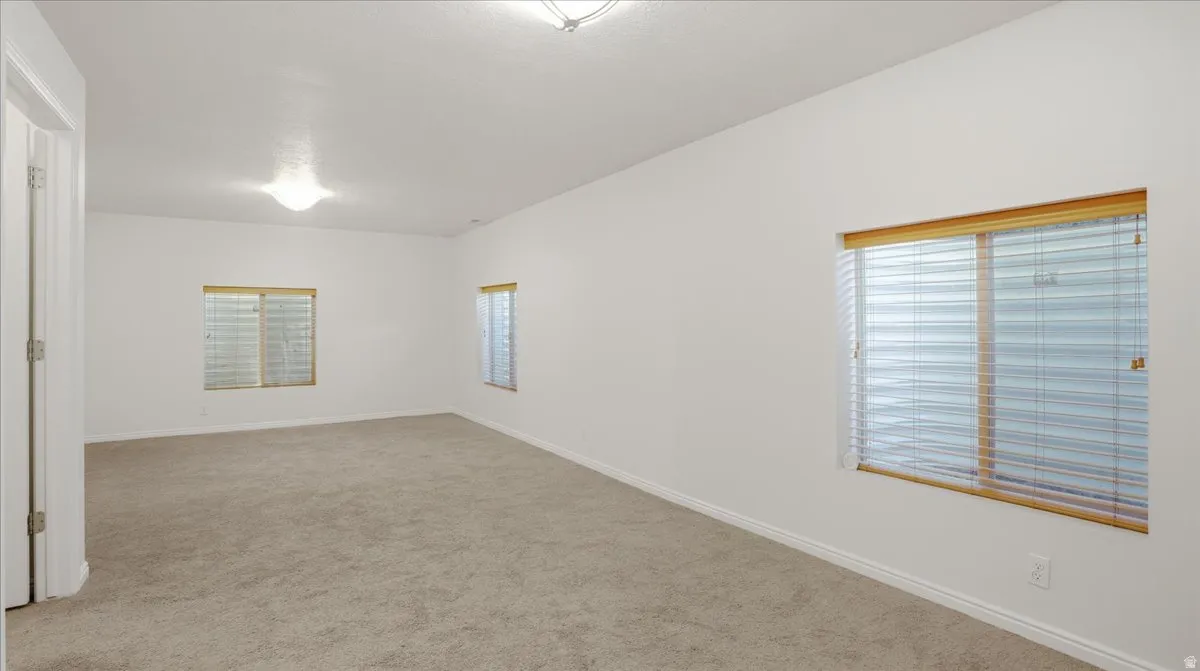 Carpeted room with white walls, multiple windows featuring blinds, and a flush mount ceiling light fixture