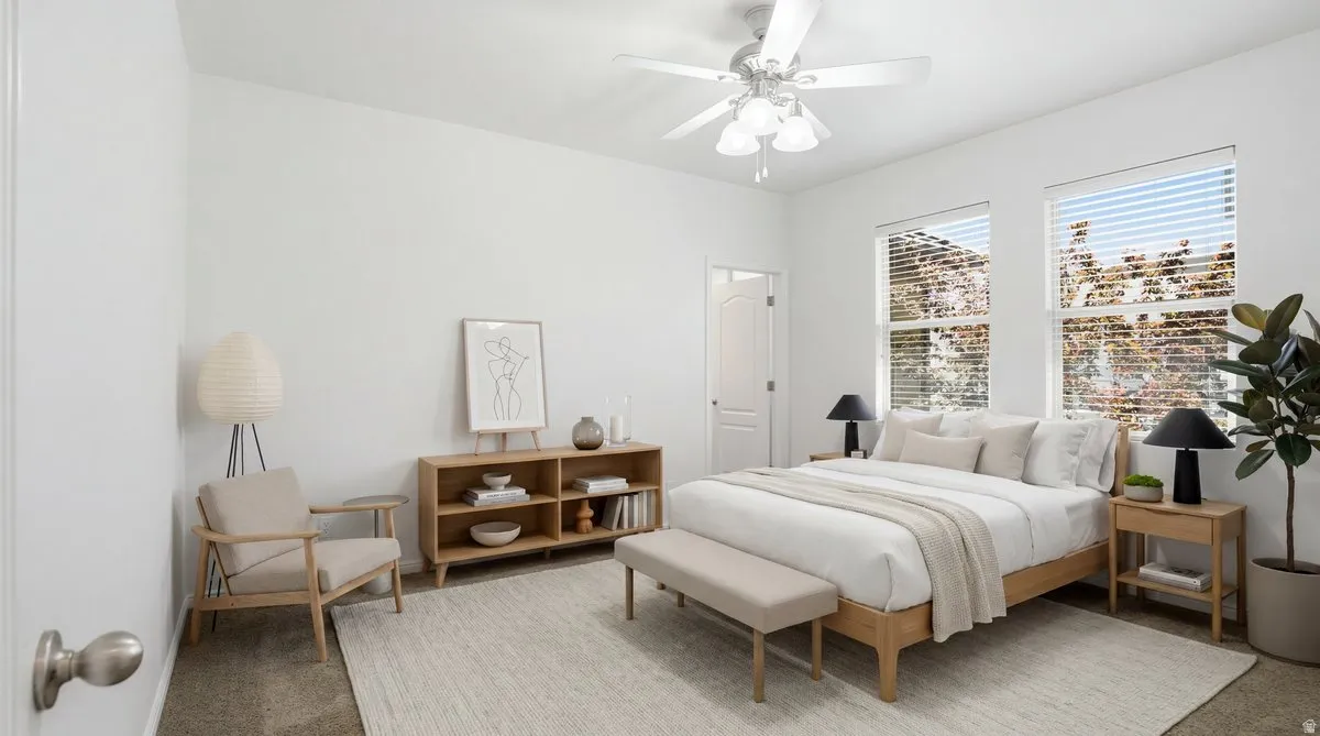 Spacious bedroom featuring dual windows with horizontal blinds, a ceiling fan with integrated lighting, and neutral-toned wall-to-wall carpeting