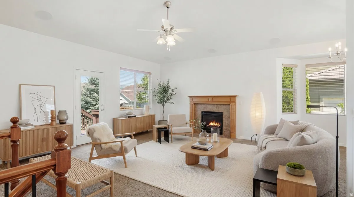 Spacious living room featuring a gas fireplace with a wood mantle and stone surround, large bay windows, a ceiling fan, and carpeted flooring
