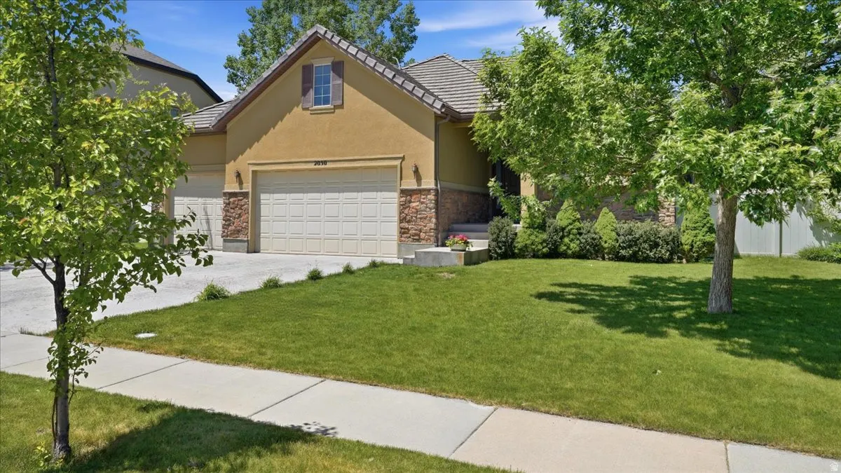 Exterior showcasing a two-car garage, an additional single-car garage, a well-maintained lawn, mature trees, and stone veneer accents