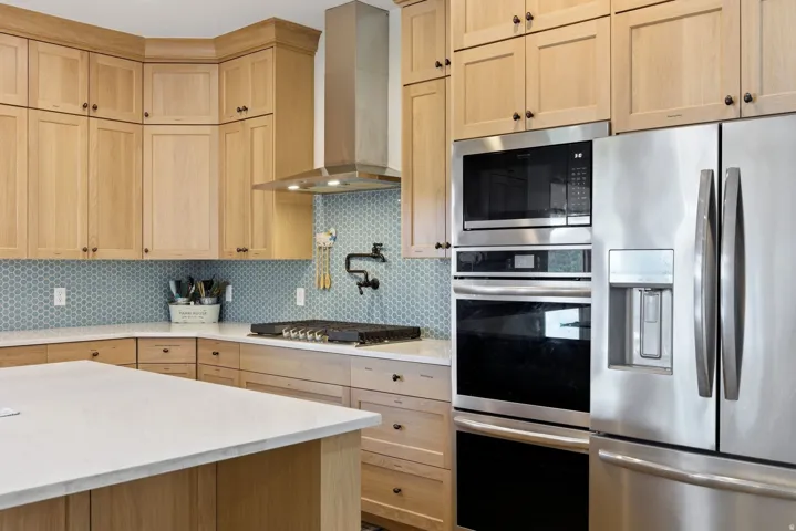 Kitchen with stainless steel appliances, light wood finish cabinetry, backsplash, and light stone countertops