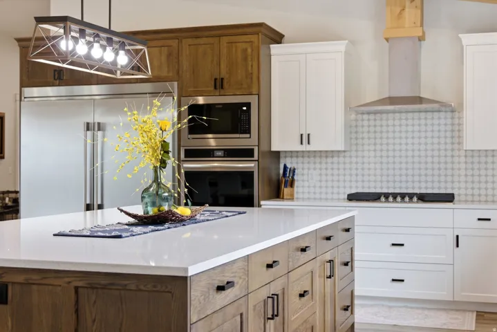 Kitchen with dual tone cabinetry, built in appliances, decorative light fixtures, light stone counters, and decorative backsplash