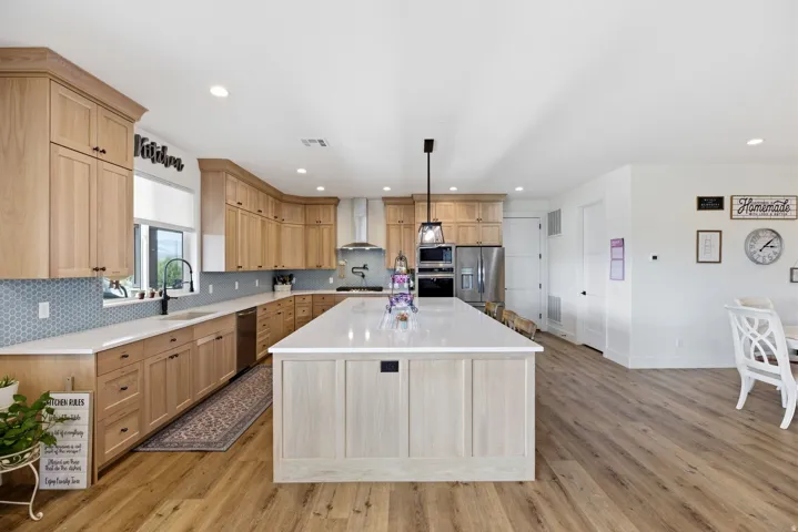 Kitchen featuring tasteful backsplash, a spacious island, light wood finished floors, light wood finish cabinets, and stainless steel appliances