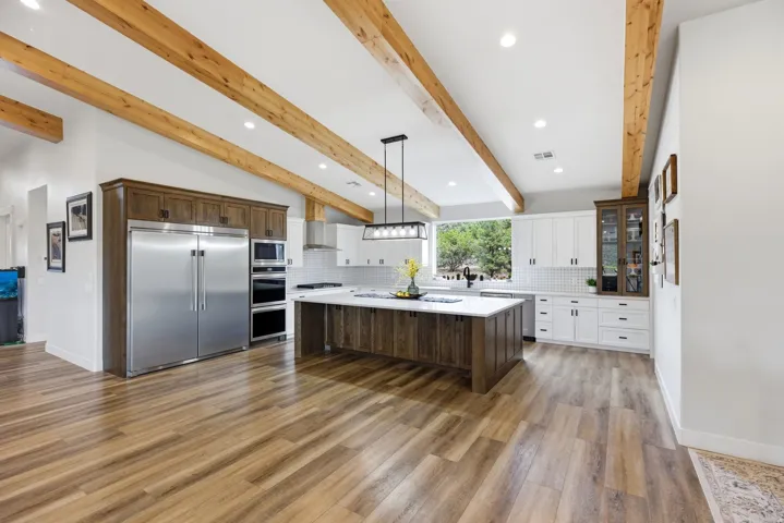 Kitchen featuring decorative backsplash, built in appliances, two tone cabinets, decorative light fixtures, and glass fronted cabinets