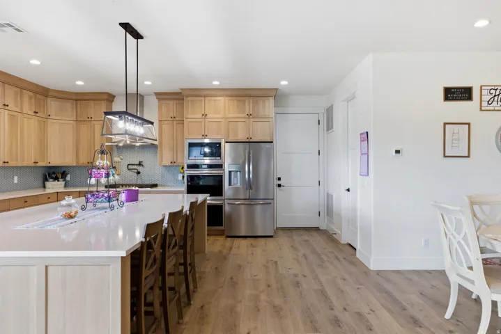 Kitchen featuring light wood finish cabinets, stainless steel appliances, a kitchen bar, light wood-type flooring, and light stone countertops