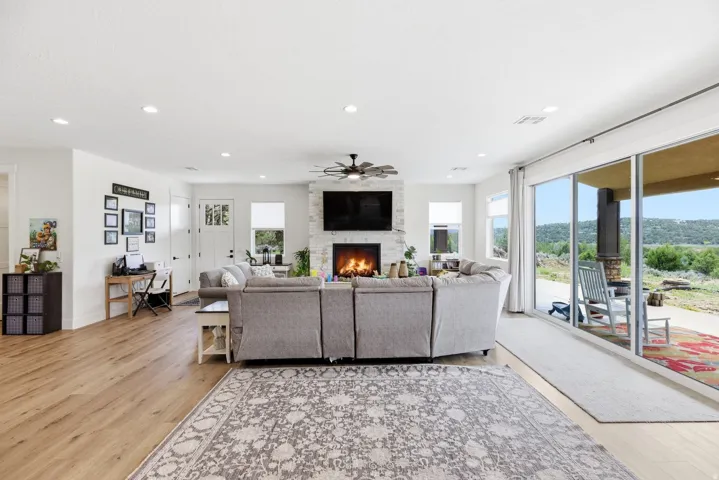 Living room featuring light wood finished floors, a ceiling fan, a desk, recessed lighting, and a fireplace