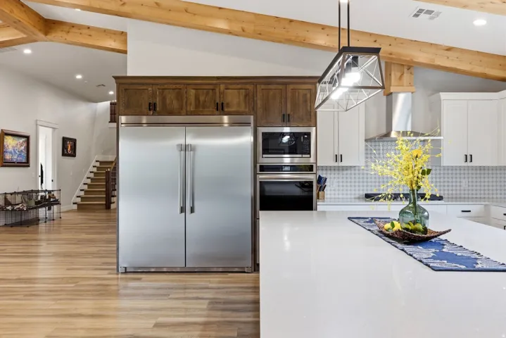 Kitchen featuring vaulted ceiling, built in appliances, light stone counters, light wood finished floors, and decorative backsplash