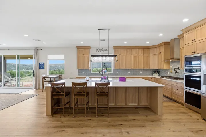 Kitchen with a breakfast bar, light wood finished floors, a large island with sink, and hanging light fixtures