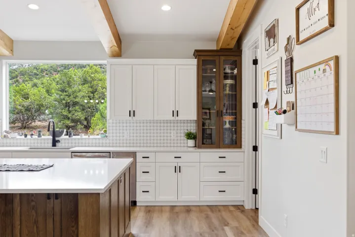 Two tone kitchen featuring two tone cabinets, beam ceiling, backsplash, glass fronted cabinets, and light wood-style flooring