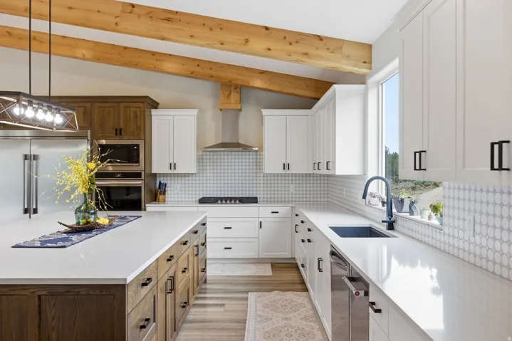 Dual tone kitchen with dual tone cabinets, vaulted ceiling with beams, hanging light fixtures, built in appliances, and light stone counters