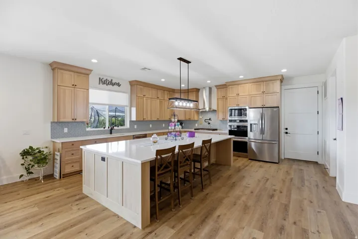 Kitchen featuring a large island, stainless steel appliances, a breakfast bar area, light wood finish cabinets, and tasteful backsplash