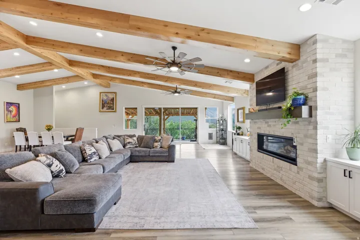 Living area with a fireplace, light wood-style floors, recessed lighting, ceiling fan, and vaulted ceiling with beams