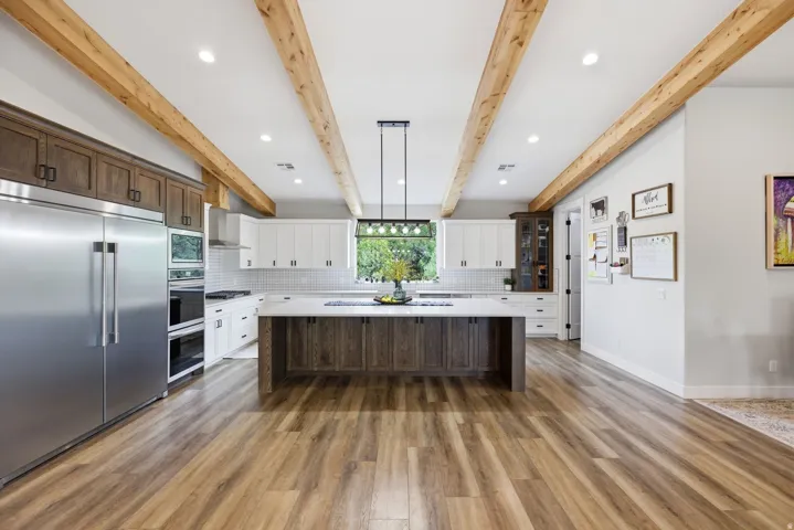 Kitchen featuring stainless steel appliances, dual tone cabinetry, decorative backsplash, a kitchen island, and light wood finished floors