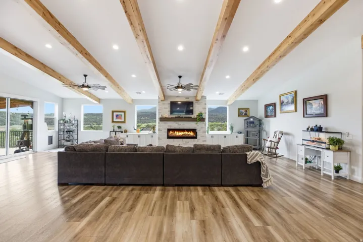 Living room featuring recessed lighting, light wood finished floors, a ceiling fan, a large fireplace, and beamed ceiling