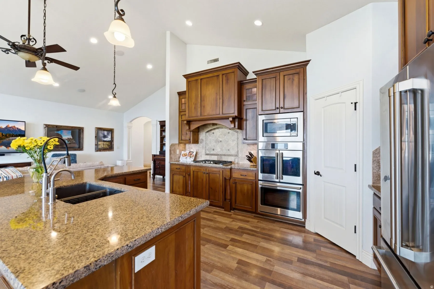 Kitchen featuring arched walkways, light stone countertops, stainless steel appliances, a ceiling fan, and vaulted ceiling