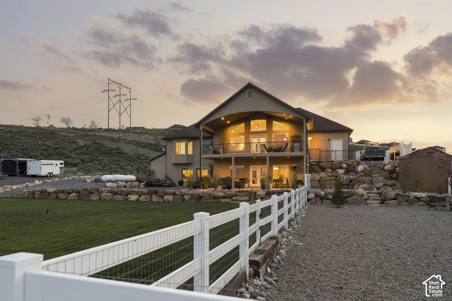 Back of house at dusk featuring a shed, stucco siding, and a balcony