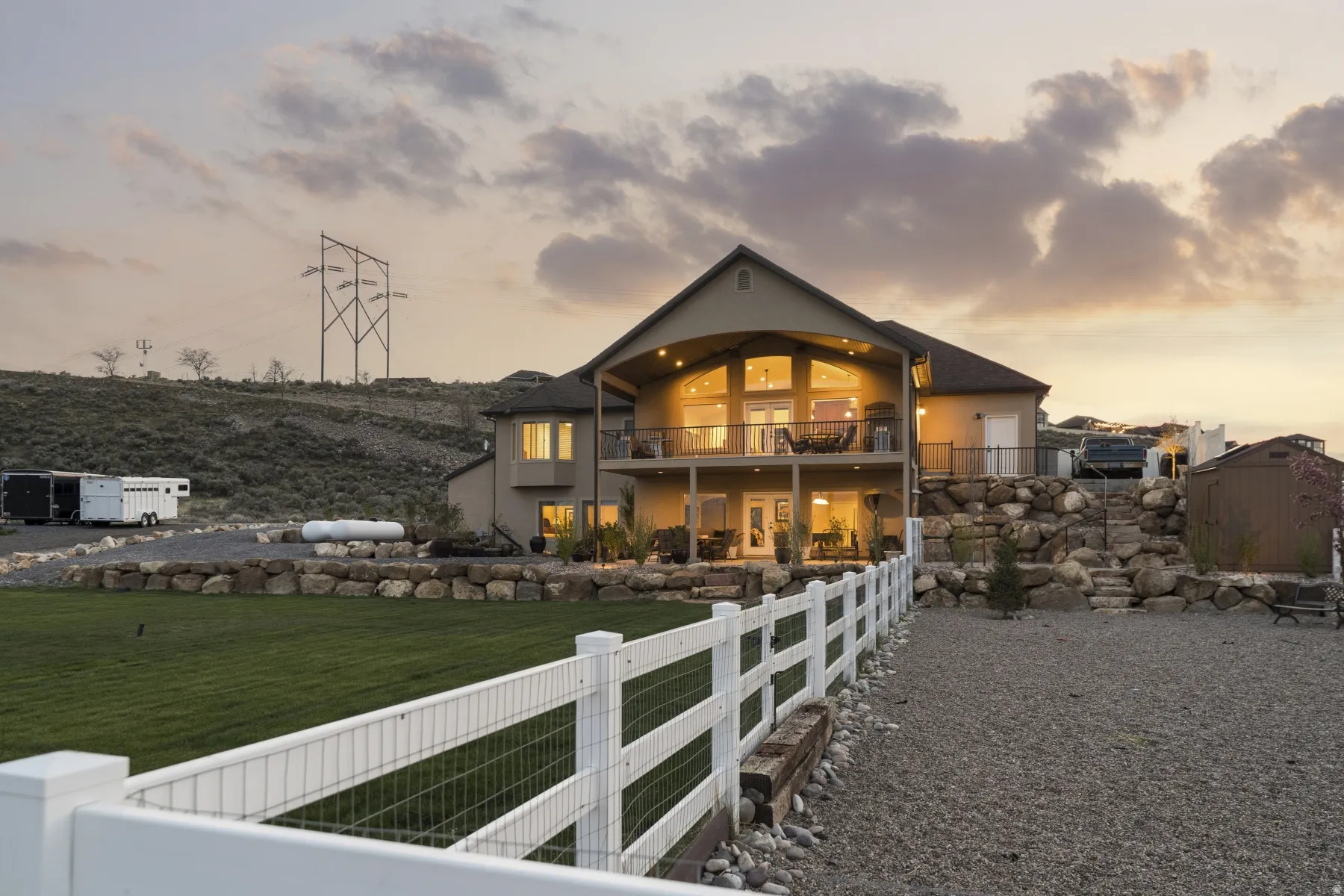 Back of house at dusk featuring a shed, stucco siding, and a balcony