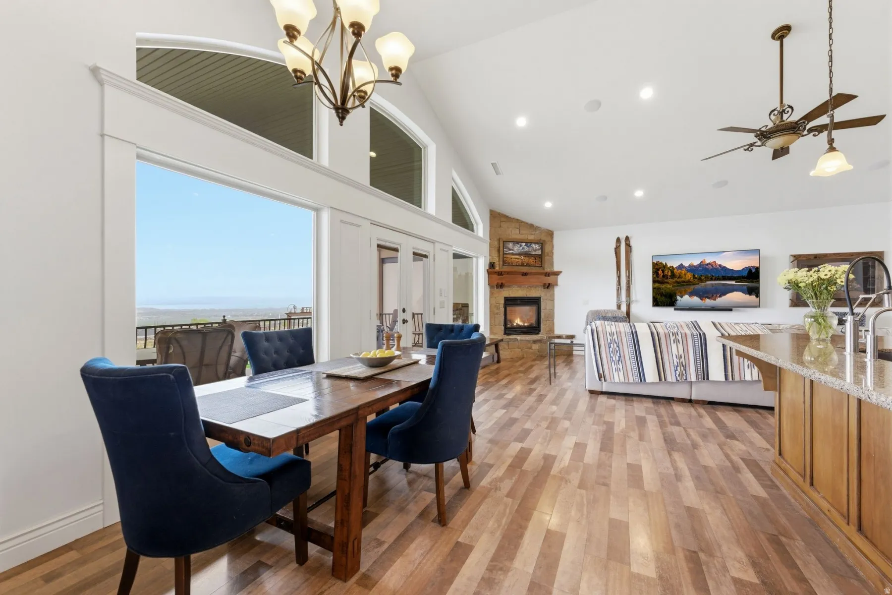 Dining room featuring light wood-type flooring, a large fireplace, vaulted ceiling, hanging lights, and a ceiling fan