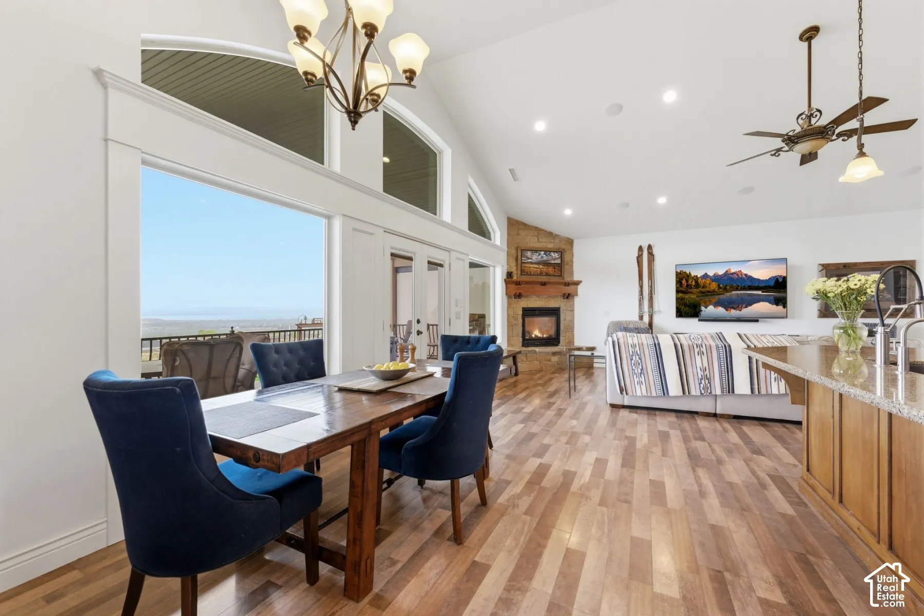 Dining room featuring light wood-type flooring, a large fireplace, vaulted ceiling, hanging lights, and a ceiling fan