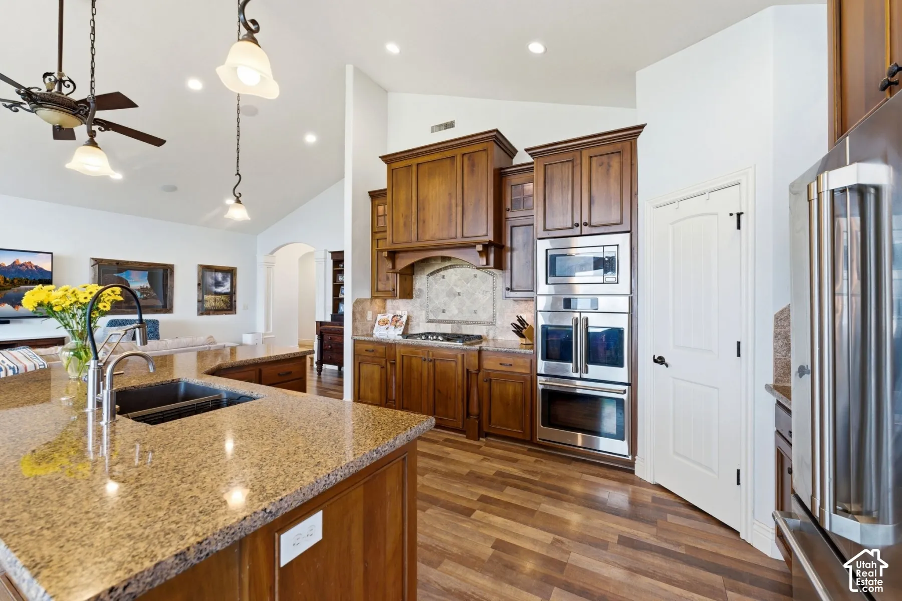 Kitchen featuring arched walkways, light stone countertops, stainless steel appliances, a ceiling fan, and vaulted ceiling