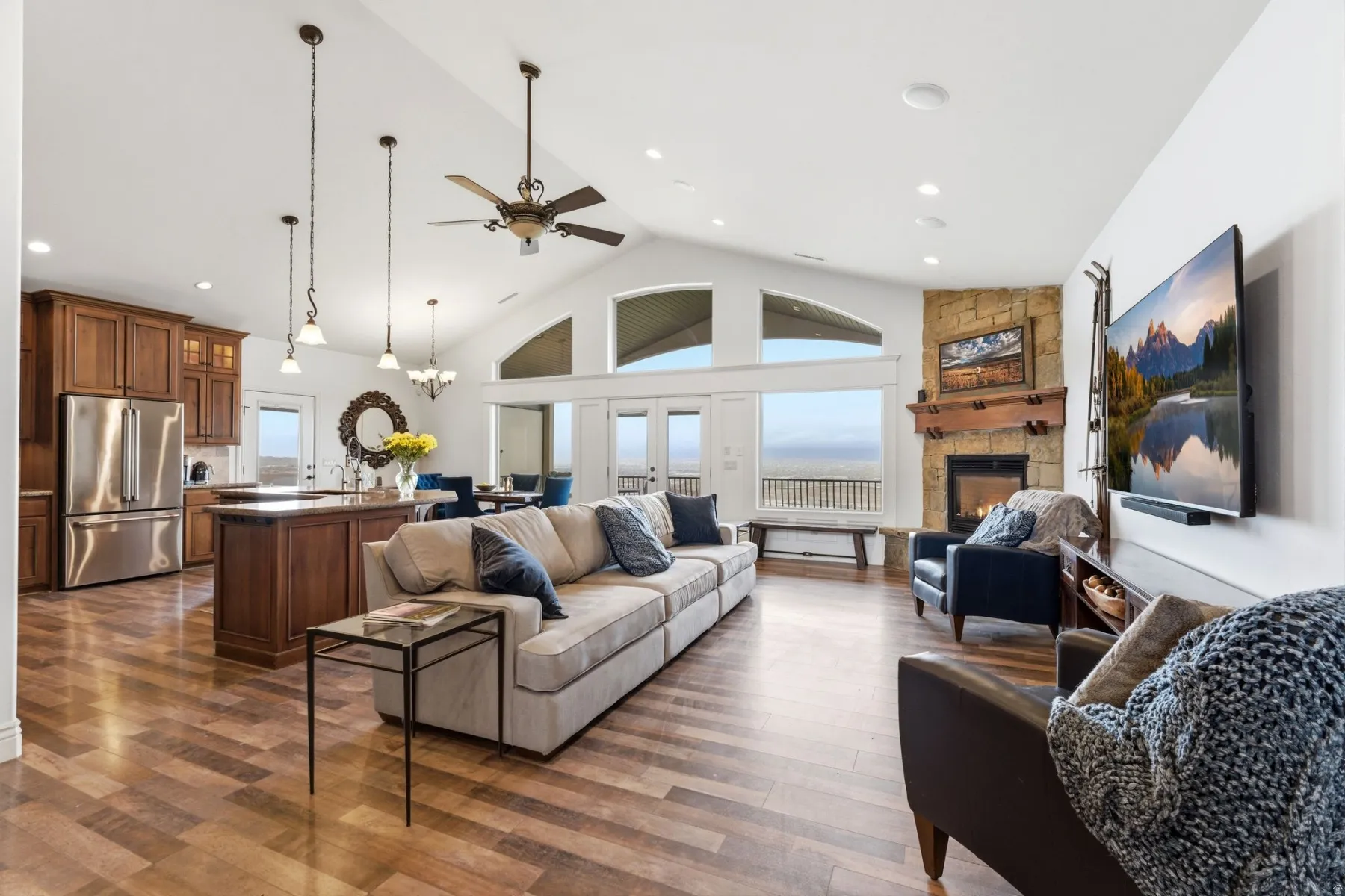 Living room with a high ceiling, a ceiling fan, dark wood-style flooring, a stone fireplace, and healthy amount of natural light