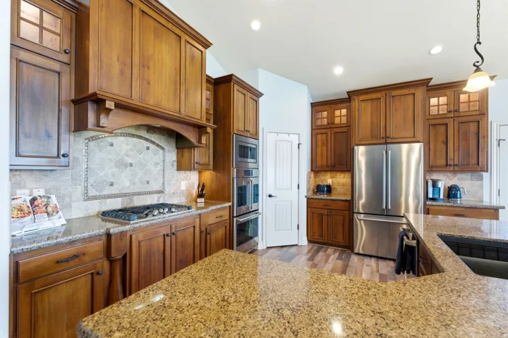 Kitchen with glass fronted cabinets, stainless steel appliances, light stone countertops, and wood finish cabinets