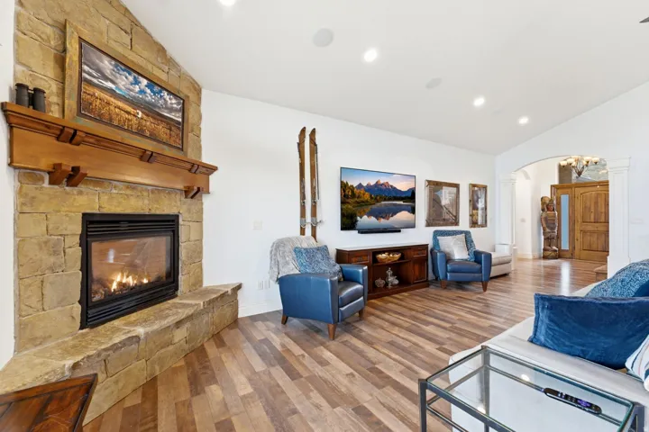 Living room with arched walkways, lofted ceiling, wood finished floors, a stone fireplace, and recessed lighting