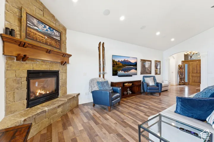 Living room with arched walkways, lofted ceiling, wood finished floors, a stone fireplace, and recessed lighting