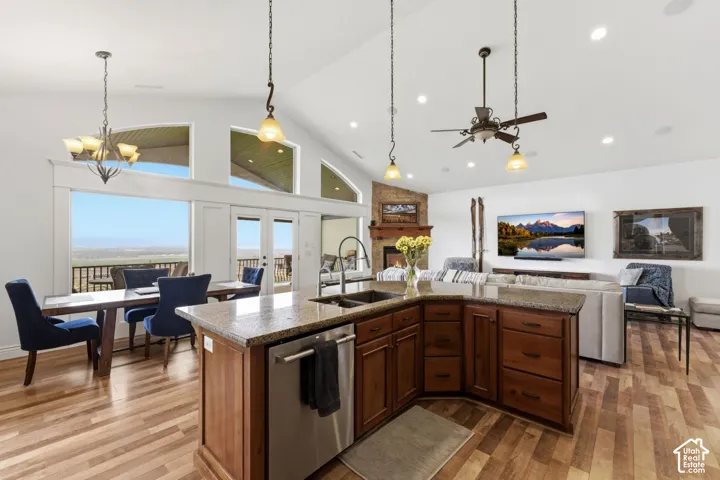 Kitchen featuring a kitchen island with sink, open floor plan, dishwasher, dark stone counters, and light wood finished floors