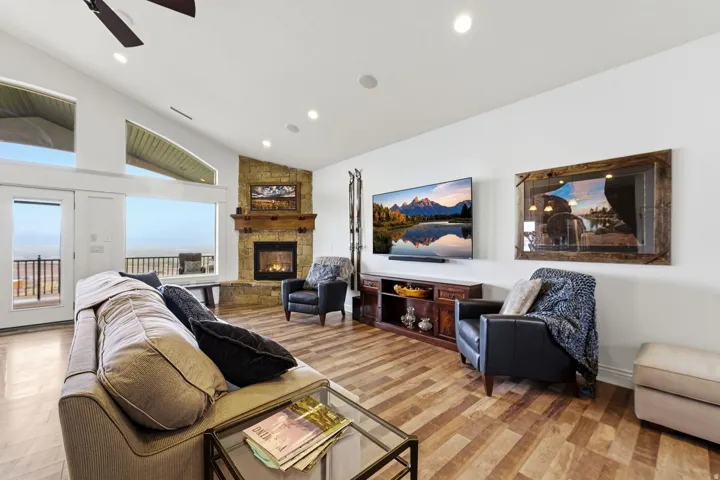 Living area with lofted ceiling, a stone fireplace, a ceiling fan, recessed lighting, and light wood-style floors