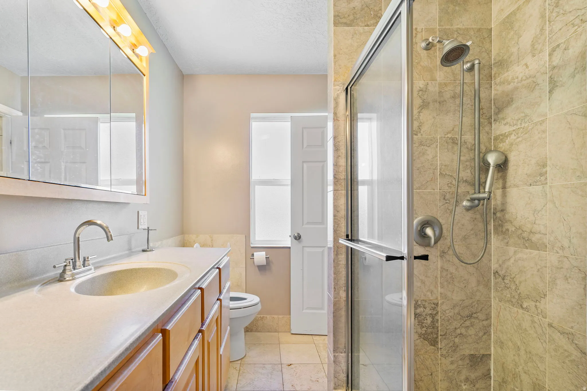 Bathroom featuring a stall shower, vanity, light tile patterned floors, and a textured ceiling