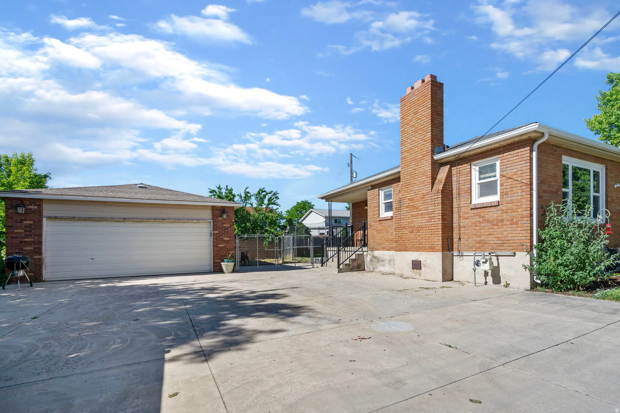 View of side of home with brick siding, a chimney, an outdoor structure, driveway, and a garage