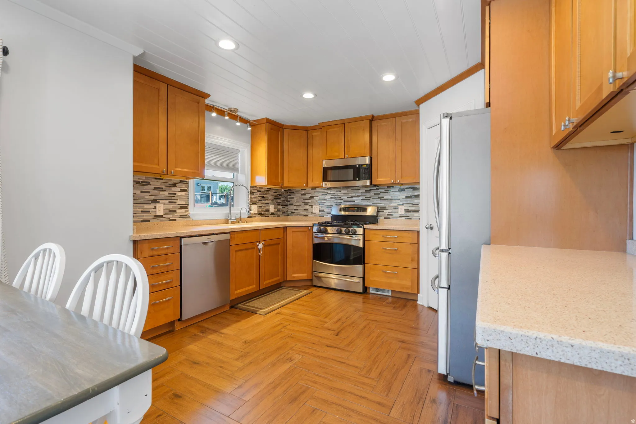 Kitchen with stainless steel appliances, parquet flooring, wood finish cabinetry, decorative backsplash, and recessed lighting