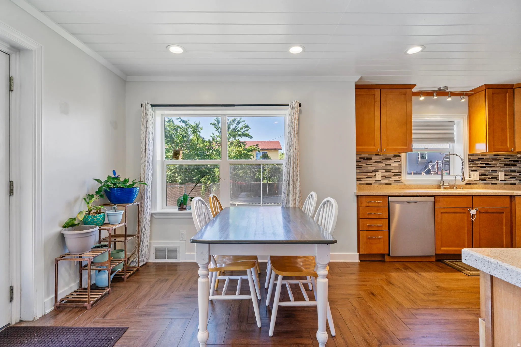 Kitchen featuring wood finish cabinetry, stainless steel dishwasher, backsplash, parquet flooring, and light stone countertops