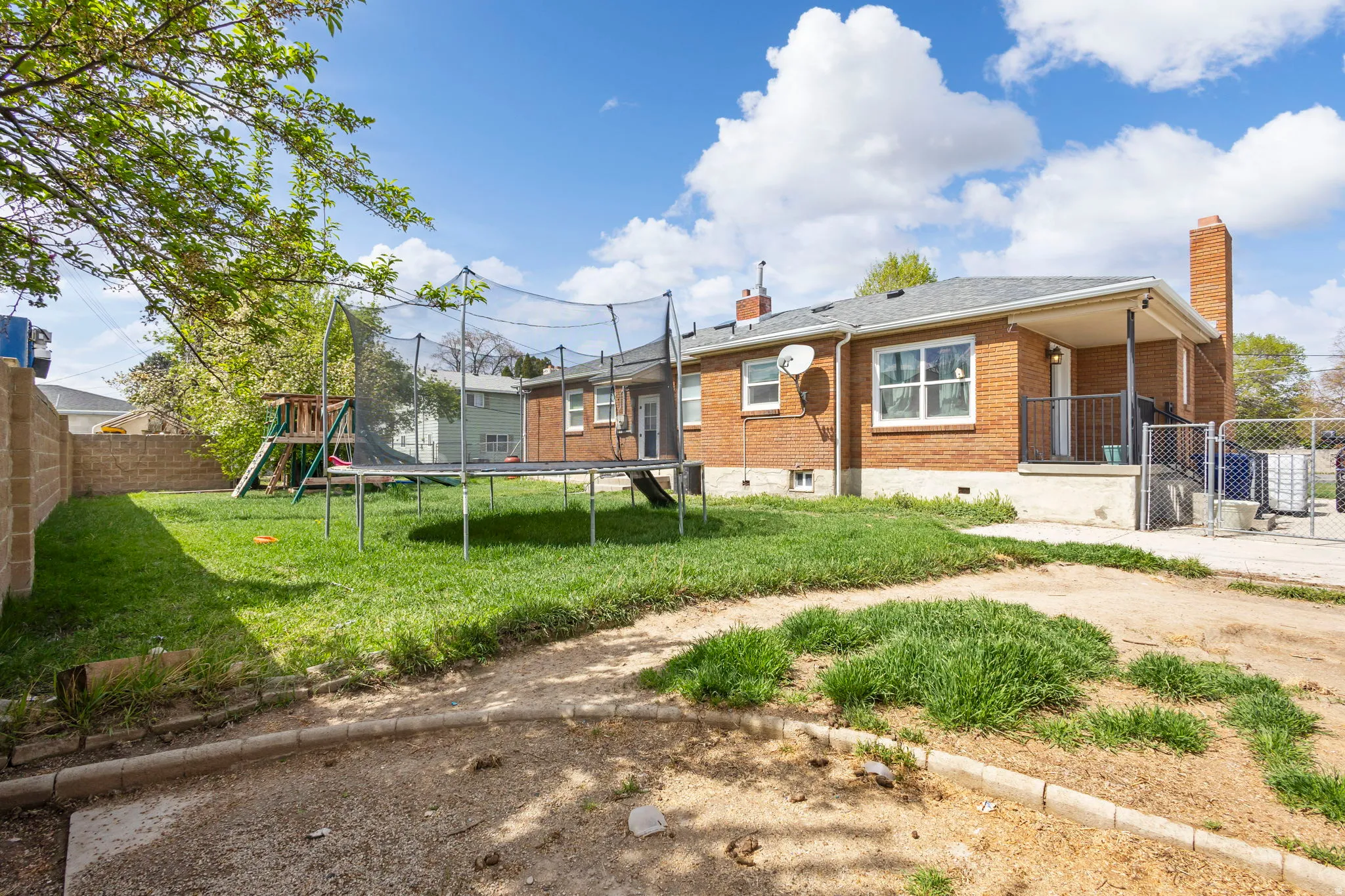 Back of property with a chimney, brick siding, a fenced backyard, a trampoline, and a playground