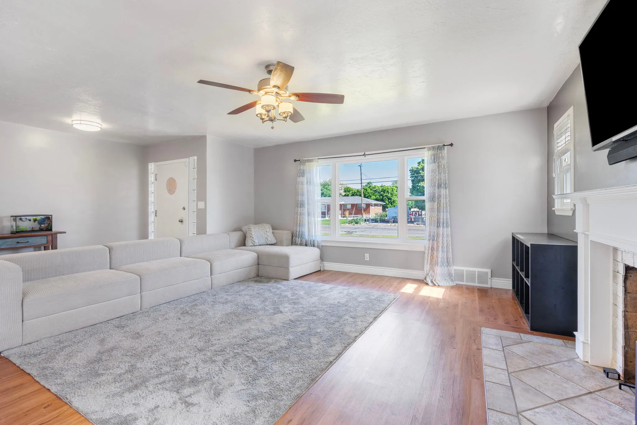 Living area with ceiling fan, light wood-style flooring, and a fireplace with flush hearth