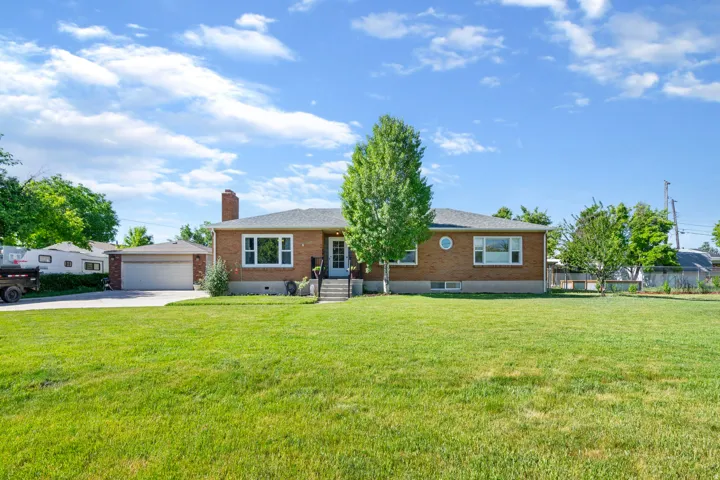 Single story home with a front yard, brick siding, a chimney, and an outdoor structure
