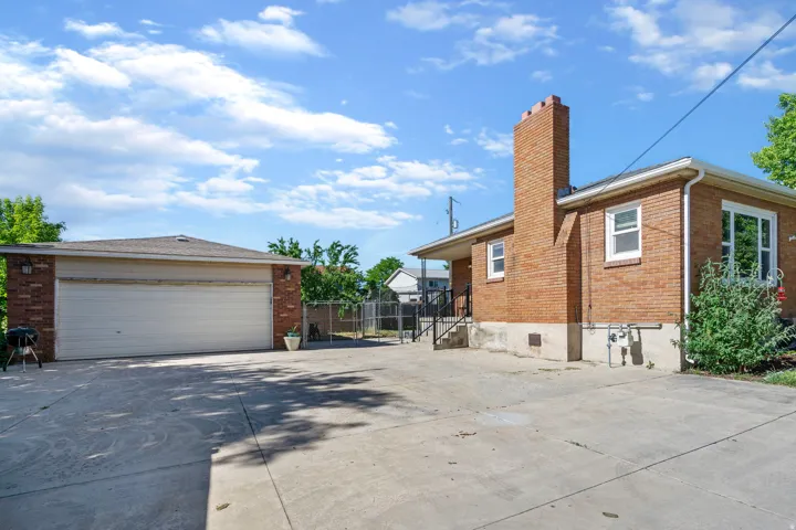 View of side of home with brick siding, a chimney, an outdoor structure, driveway, and a garage