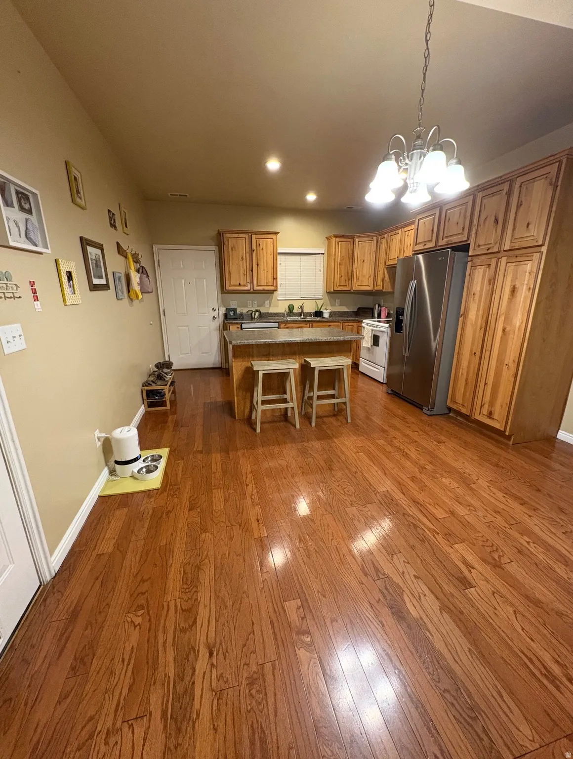 Kitchen with suspended lighting, wood finish cabinetry, stainless steel fridge, dark wood-style flooring, and a breakfast bar