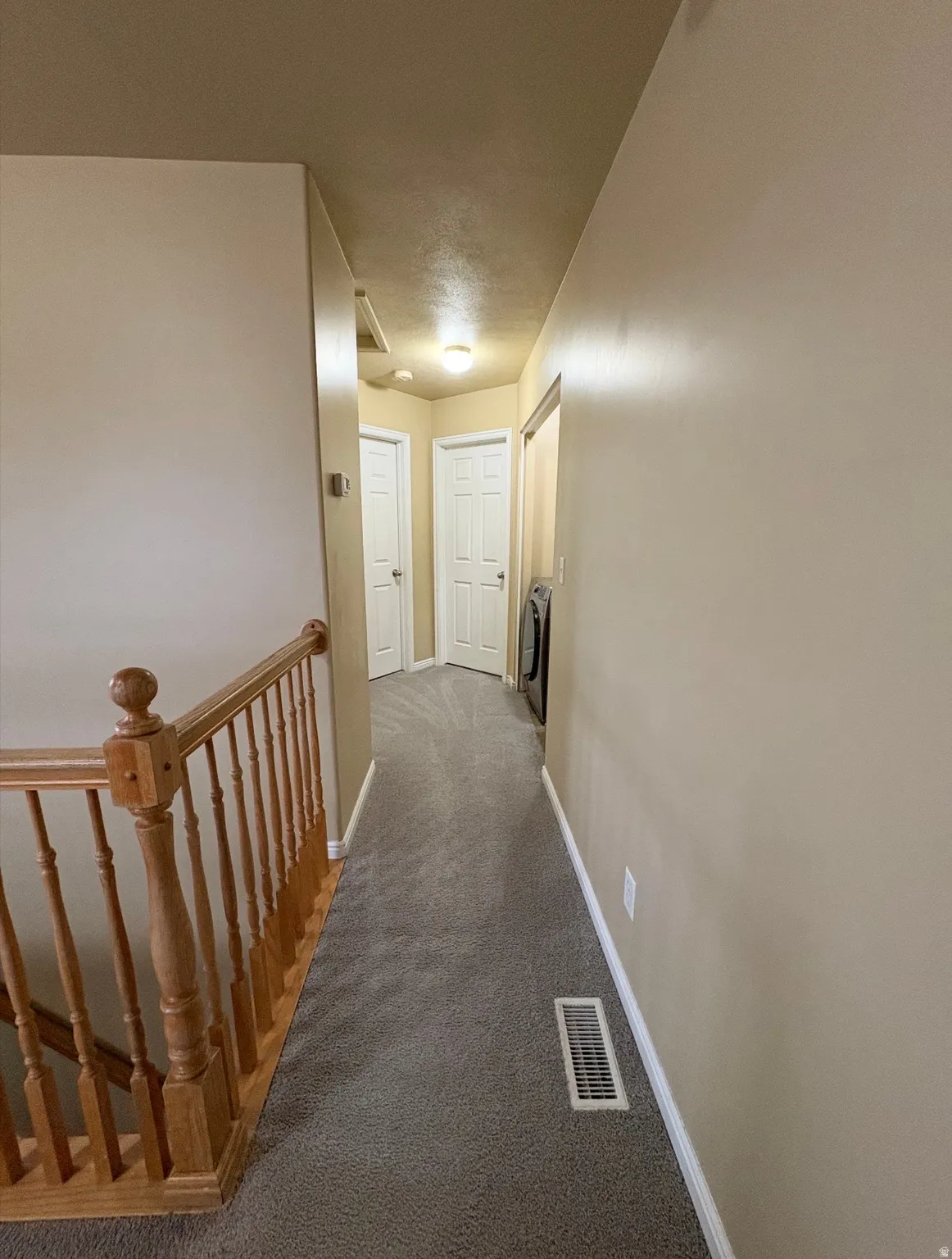 Hallway with dark carpet and an upstairs landing