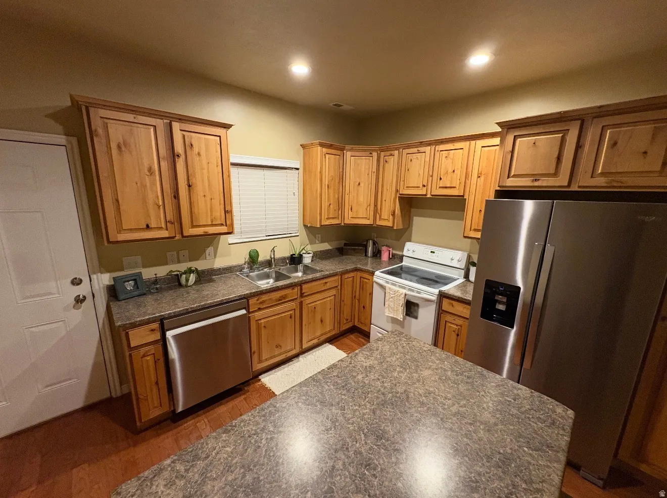 Kitchen featuring stainless steel appliances, dark countertops, dark wood-style flooring, wood finish cabinetry, and recessed lighting